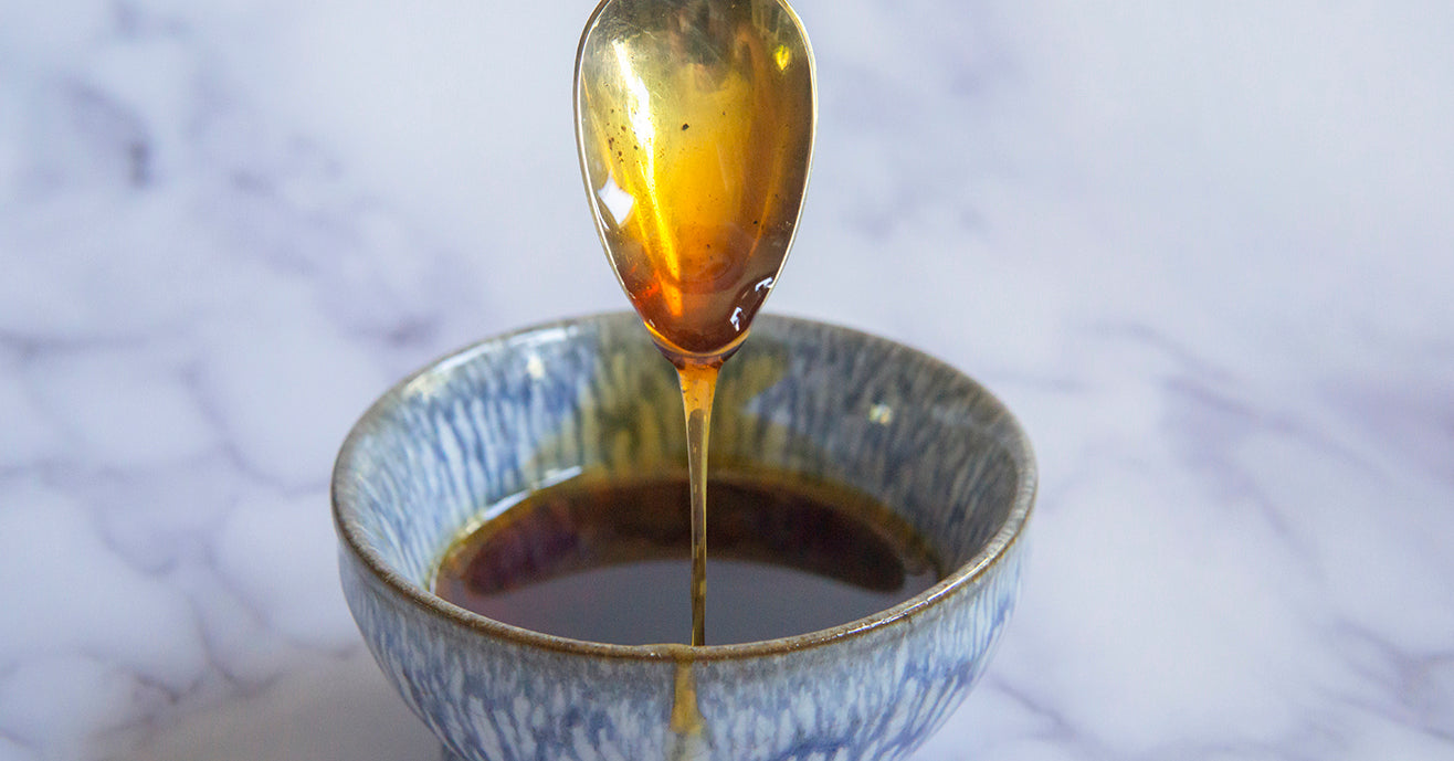 Tea infused amber colored syrup drizzling off spoon into blue ceramic bowl. 