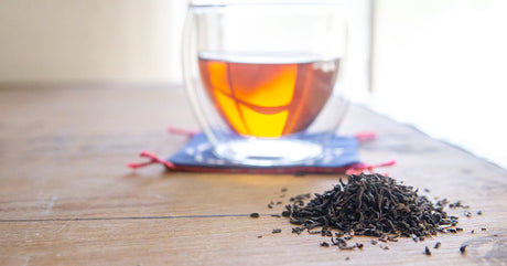 Black tea leaves next to a cup of tea on a Himalayan pink salt cutting board.