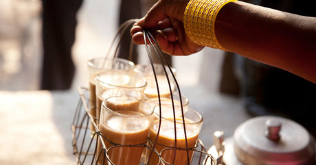 Man  serving chai with several cups in a metal basket in India